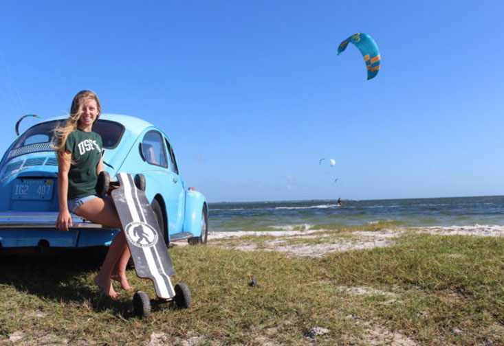 Entrepreneurship Student Makenzie Black holding a cargo trailer while leaning against a car parked on a beach