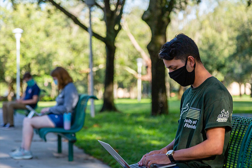 Students wearing masks while sitting on benches while working on their laptops