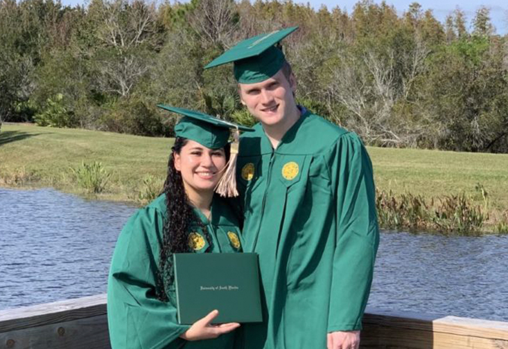 Michael and Jacqueline Ray wearing graduation cap and gowns displaying their diploma