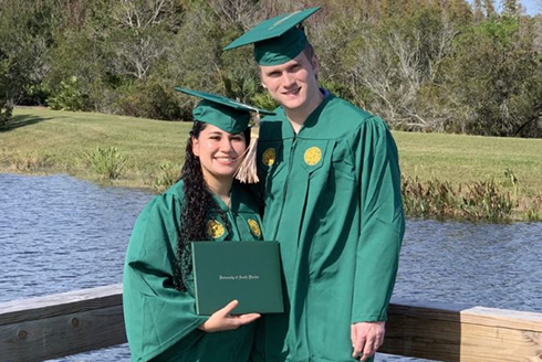 Michael and Jacqueline Ray wearing graduation cap and gowns displaying their diploma