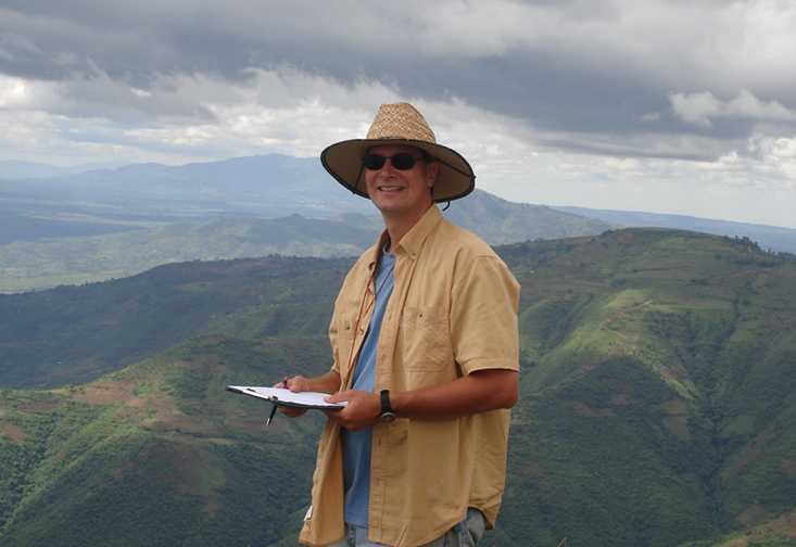 John Arthur on the top of a mountain with a mountain range in the background
