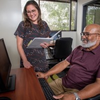 A man sitting at a computer with a woman standing next to him.