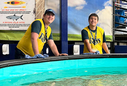 Joseph Davis and Sam Essman wearing Rays jerseys standing in frontn of the touch tank at Tropicana field.