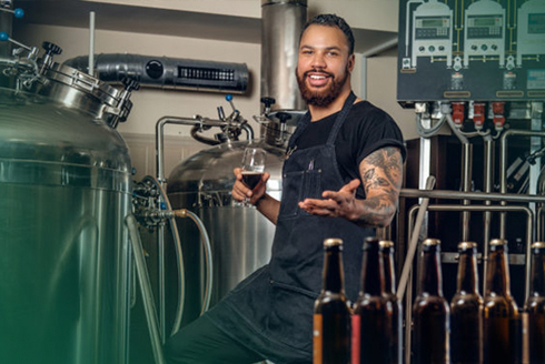 Man holding a glass of beer with several beer bottles in front of him