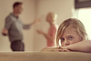 child looking into camera with parents in the background