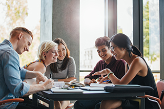 Students sitting around a table smiling and talking with notebooks on the table in front of them